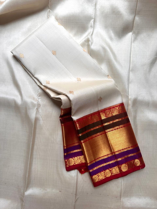 Draped ivory Pure Kanchipuram silk saree showing scattered gold buttas and a broad gold zari border with red and purple accents