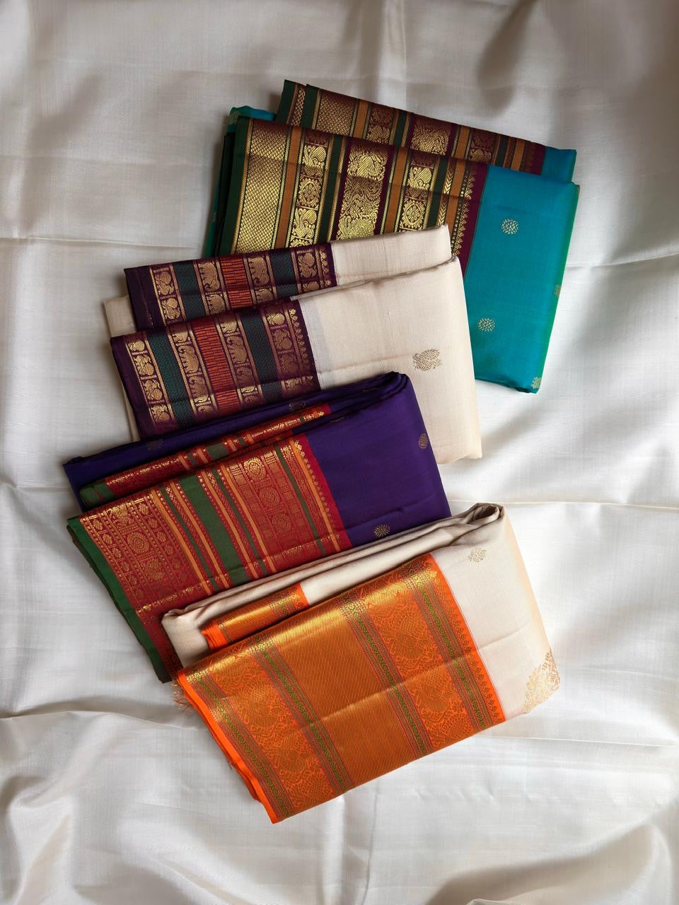Folded Warm Ivory Varisaipet silk showing petite zari buttas and richly layered purple green gold border.