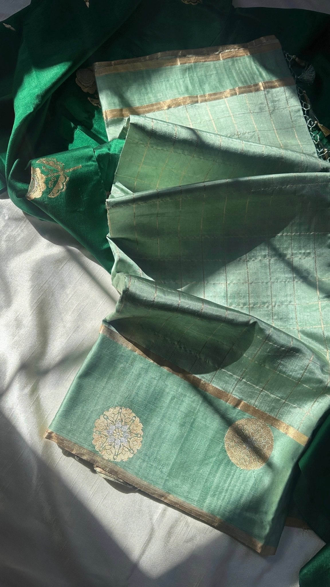 Pure silk Kanchipuram saree in sage green with fine zari checks and antique gold circular buttas along the border, photographed in soft natural light.