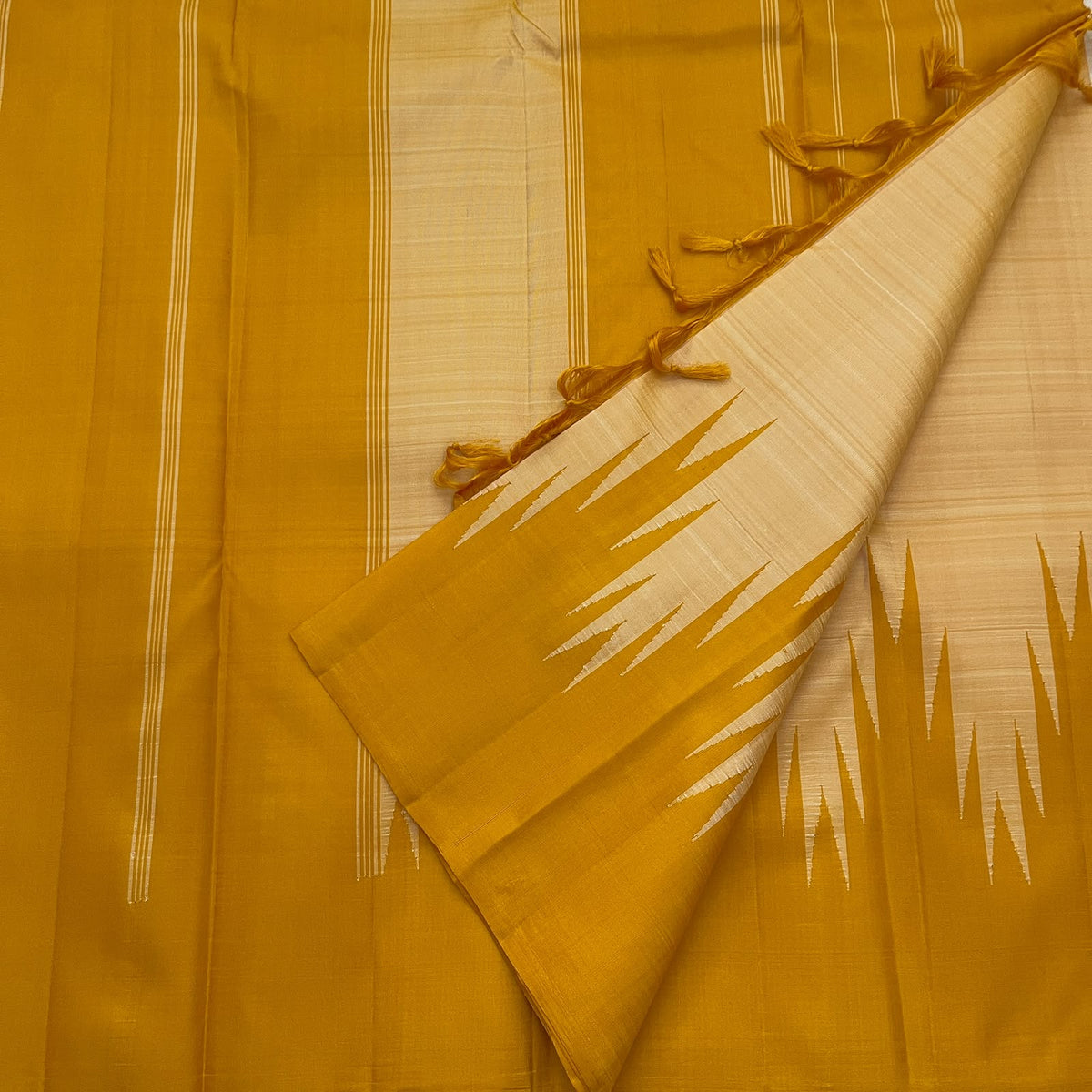 Golden mustard and sandalwood ivory pure silk Kanchipuram saree folded to showcase the traditional Thazampoo Reku Korvai design.