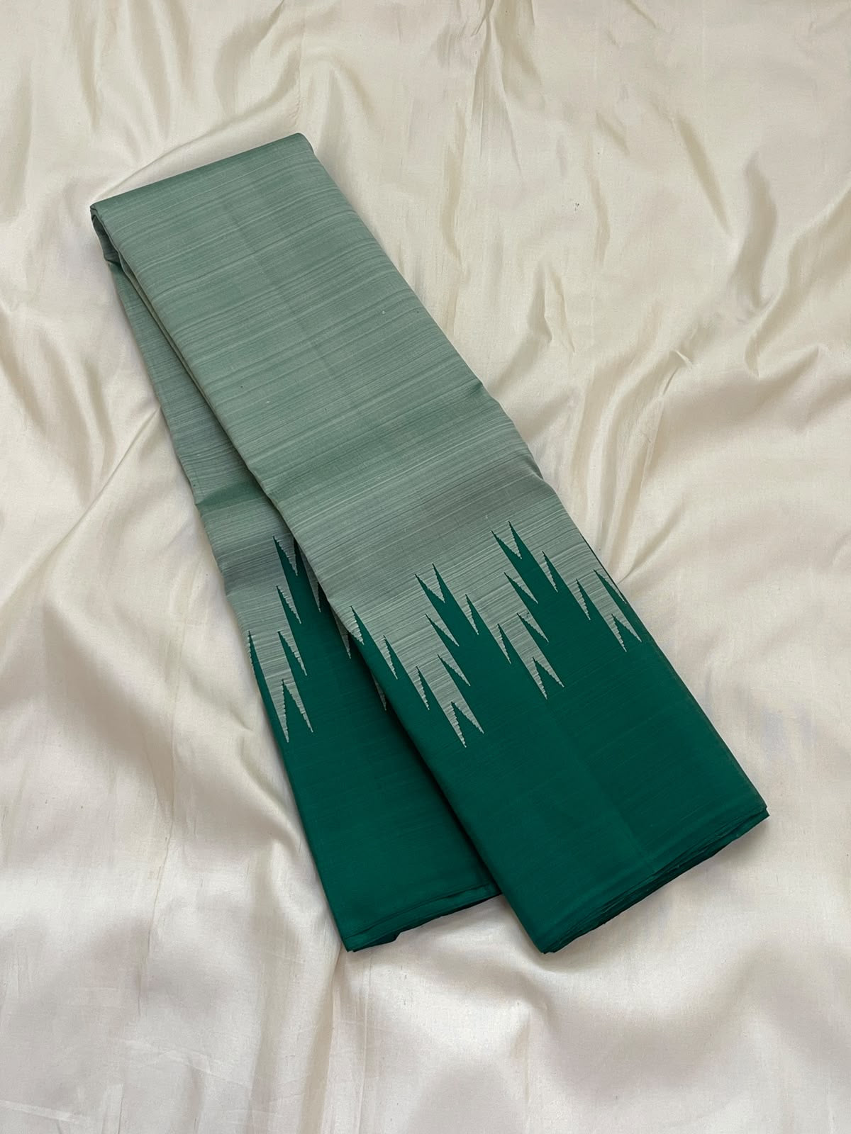 Deep emerald green and misty sage pure silk Kanchipuram saree folded to display dramatic Thazampoo Reku Korvai pointed border detailing.