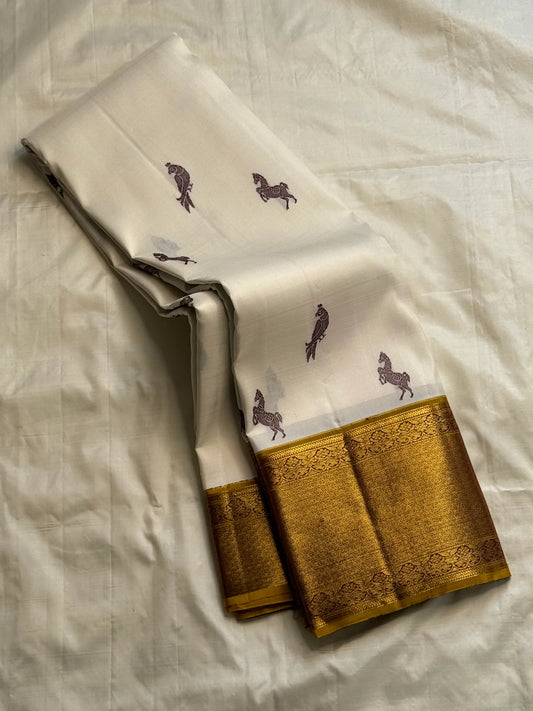 Folded ivory Kanchipuram silk saree with maroon horse and parrot buttas and rich antique-gold zari border on cream backdrop
