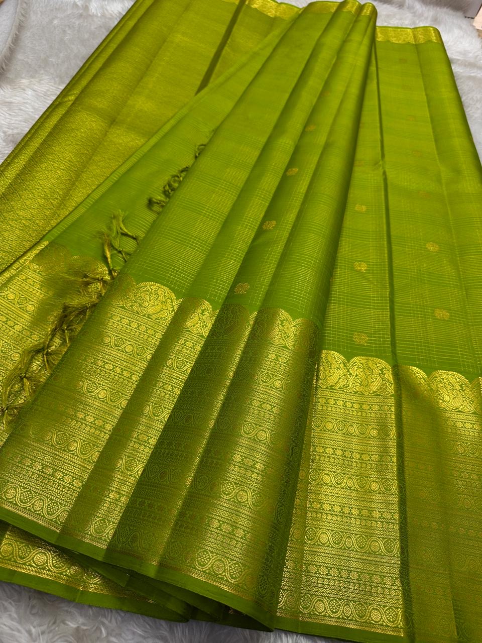 A radiant parrot green Kanchipuram silk saree that dazzles. The body features a delicate grid-like zari weave with small gold buttas scattered. The rich gold zari pallu stands out with grand temple-inspired arches and intricate motifs.