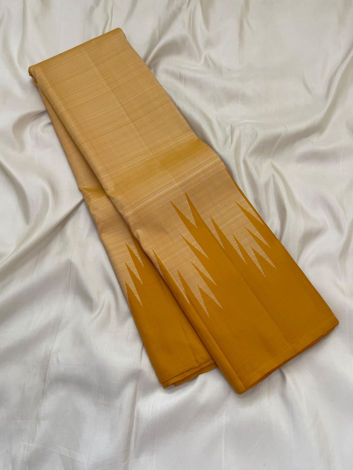 Traditional Thazampoo Reku Korvai border with elongated sandalwood-ivory triangular forms against golden mustard silk.