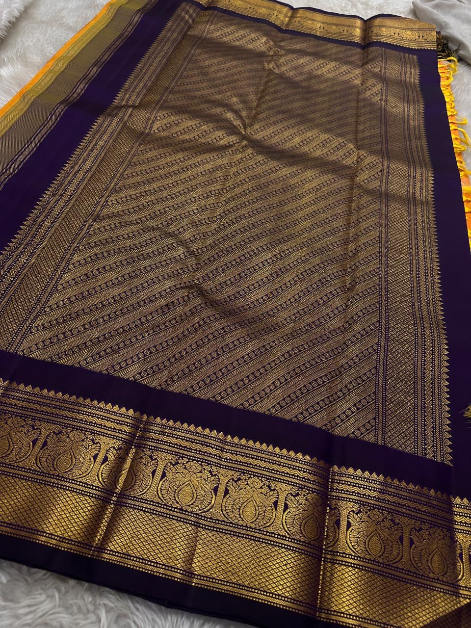 Pure Kanchipuram Silk Saree – Saffron-Orange Body with Gold Zari Paisley Buttas
Contrast Deep Purple Korvai Borders with Intricate Temple & Floral Motifs
Grand Purple Zari Pallu with Diagonal zariWeave . Silk mark , ships in 2 weeks