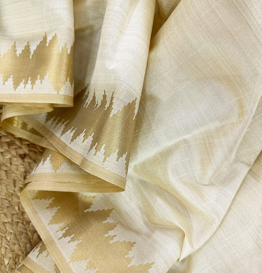 Minimal yet majestic, this ivory-beige silk saree is a celebration of simplicity and sophistication. The body is plain and luminous,  texture of the silk shines through. golden zari border with a sharp, zigzag temple-inspired pattern - perfect for Onam