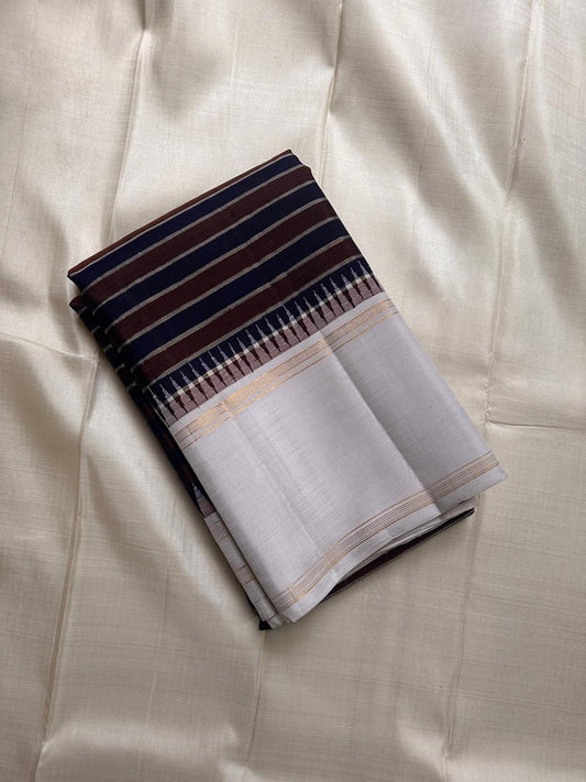 The most unique striped pure silk Kanchipuram with the faintest dove grey border with thazampoo reku , a body of navy and coffee brown stripes separated by distinct zari work ! Truly stunning and rare