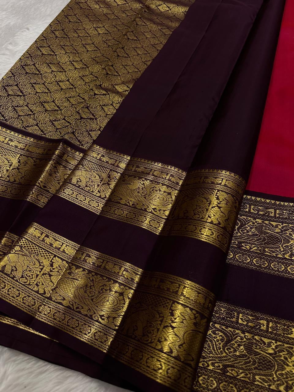 A regal  shot tomato red pink Kanchipuram silk saree features elegant chakram and mayil gold zari buttas woven across the body. Brown contrast rettapet border and Pallu vanasringaram details