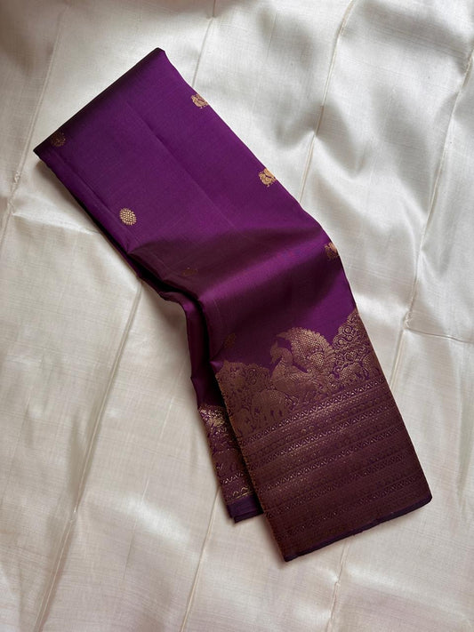 Swarna
Majestic Purple Pure Silk Kanchipuram Saree with Broad Varisaipet Zari Border,Intricately Woven Peacock and Elephant Motifs alongside border . Peacock motifs all over.
