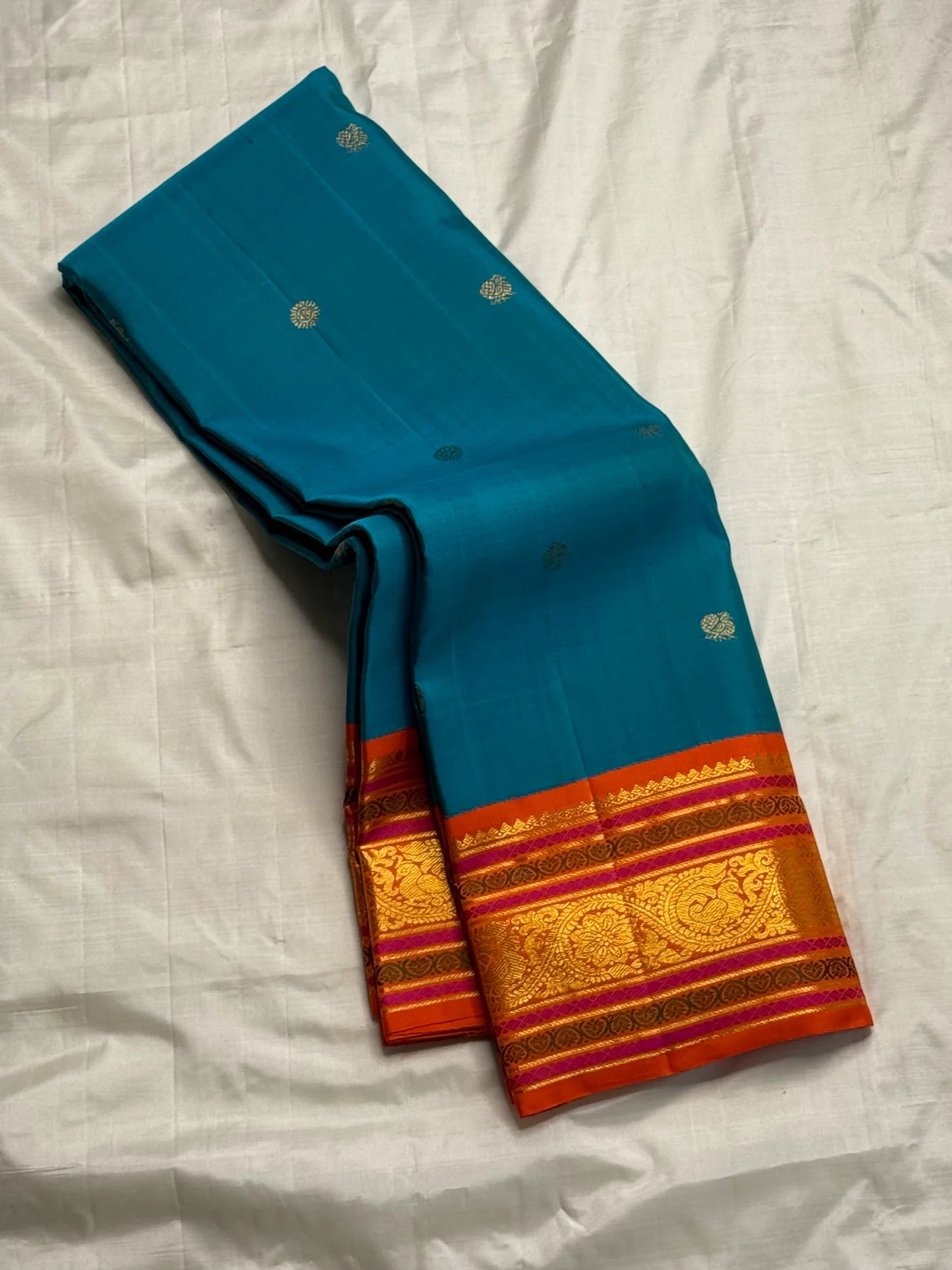 Aazhi Teal — Pure Kanchipuram Silk Saree
Teal body with silver-zari rosette buttas and korvai kavi–magenta borders in gold-zari brocade.
Silk Mark Certified • Free Shipping within USA • Ships in Two Weeks ✅
