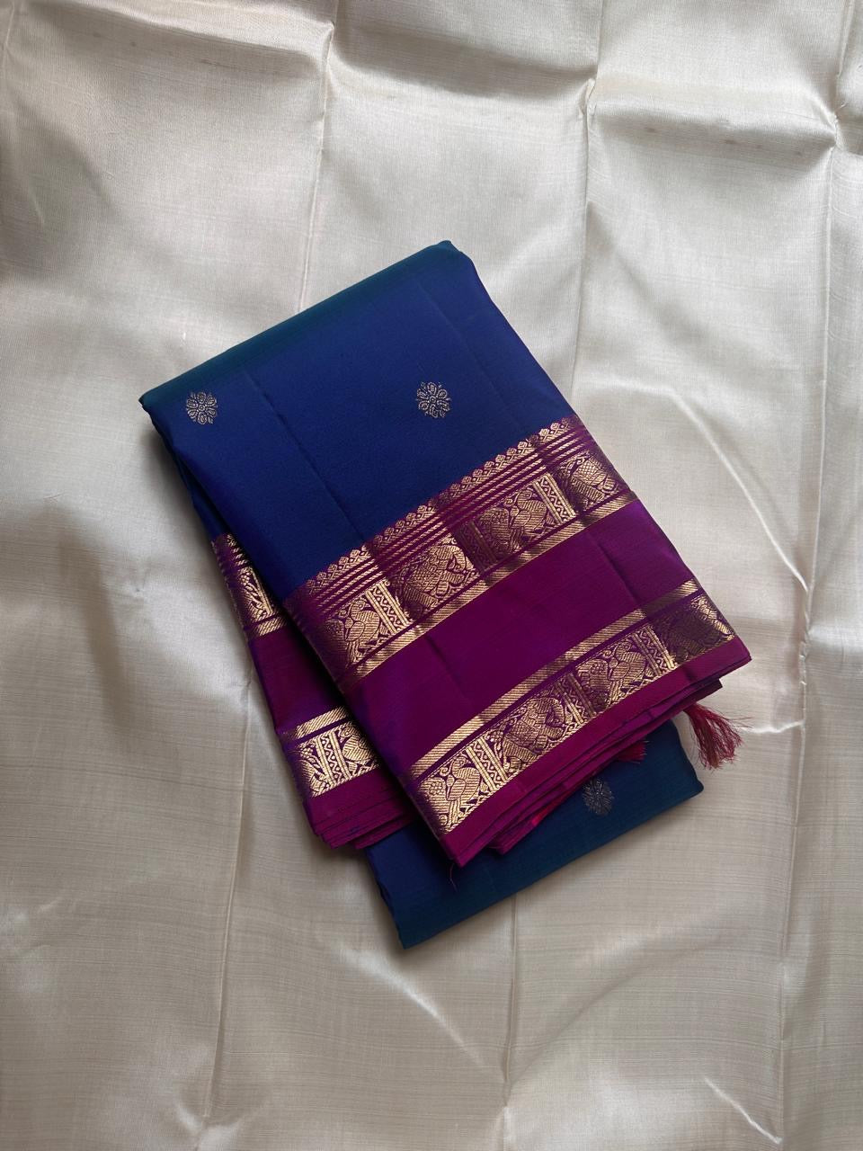Purple Allure – Pure Kanchipuram Silk Saree
Peacock-blue body adorned with petite zari floral buttas 🌸
Contrast royal-purple border with grand elephant procession 🐘
Rich zari brocade pallu in floral motifs ✨

Silk Mark Certified, delivery in 2 weeks