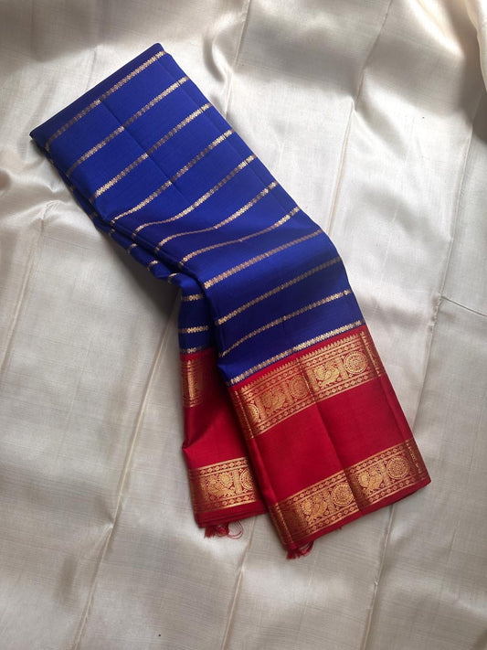 Meera – A Living Raga in Kanchipuram Silk: Draped in Crimson and Iconic MS Blue, Adorned with Gold Zari Seer, Muthu Borders, and Peacocks and kamalam , Woven in the Spirit of Classical Grace and Devotion