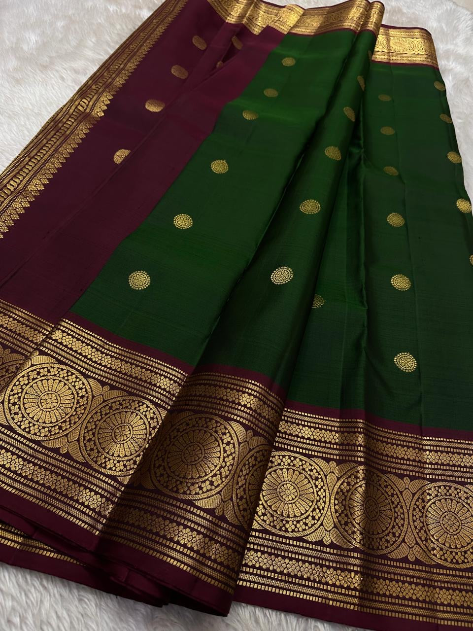Pachai Butta – Pure Kanchipuram Silk Saree
Emerald silk scattered with radiant buttas.
A wine korvai border rich in gaja artistry.
Floral medallions glow in antique-gold zari.

Silk Mark Certified, delivery in 2 weeks