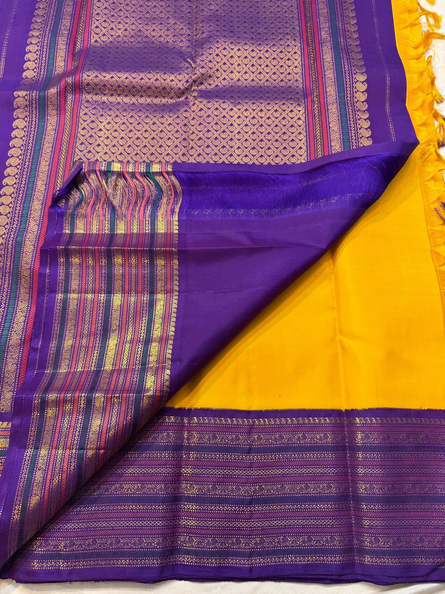 Swarna Kanakam Mayil Chakram — Pure Kanchipuram Silk Saree
Radiant turmeric-gold body adorned with silk-thread mayil and chakram buttas, framed by a regal vadamalli zari-woven korvai border and rich purple pallu.
Silk Mark Certified • Blouse Stitching Ava