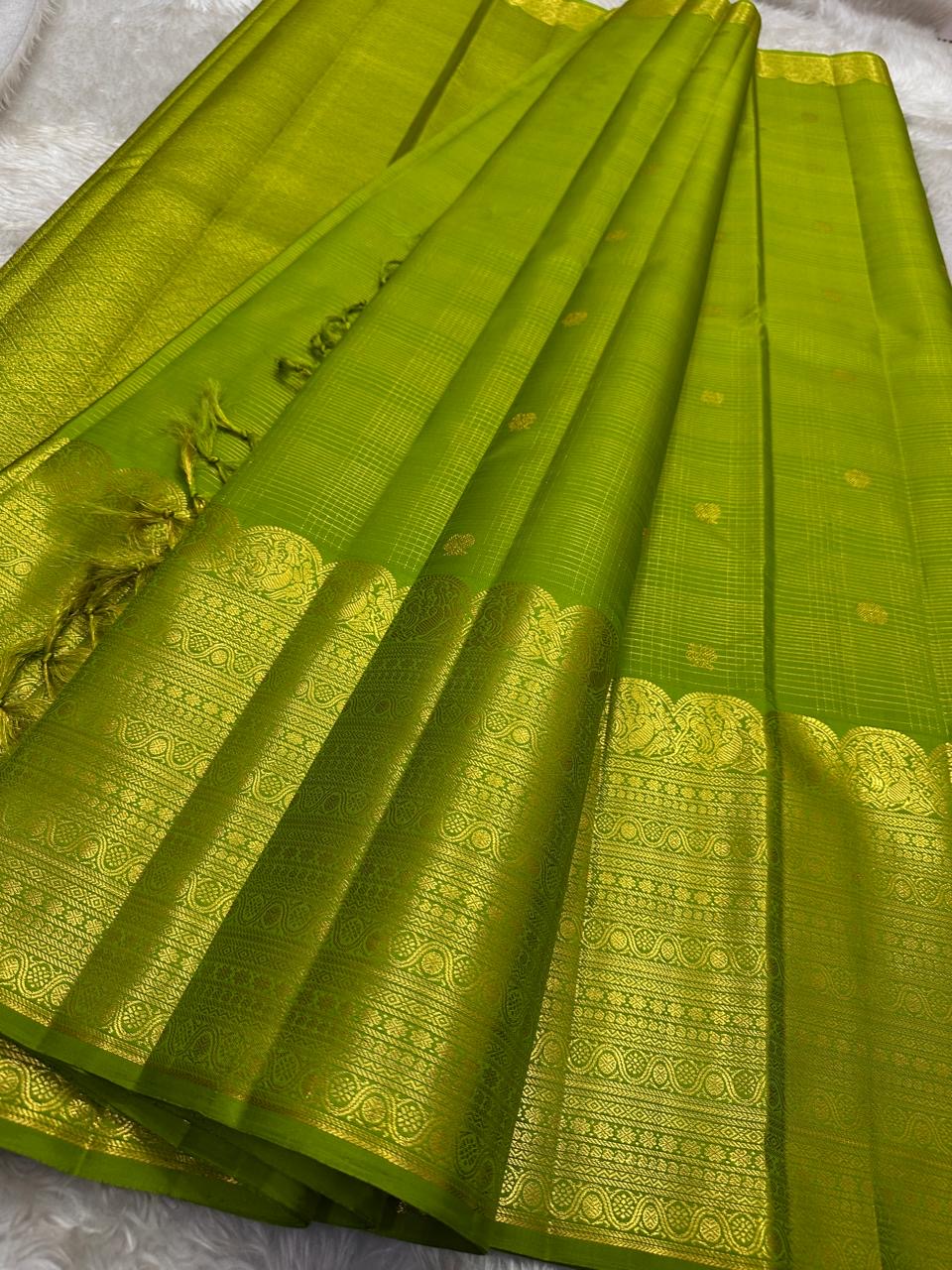 A radiant parrot green Kanchipuram silk saree that dazzles. The body features a delicate grid-like zari weave with small gold buttas scattered. The rich gold zari pallu stands out with grand temple-inspired arches and intricate motifs.