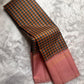 Nirai – A Madras-Inspired Kanchipuram Silk in Amber & Pastel Pink.
Woven with fine podi kattam checks in black, amber orange, and grey.
The pastel pink border with pillayar moggu detailing adds softness, with a  seer zari pallu