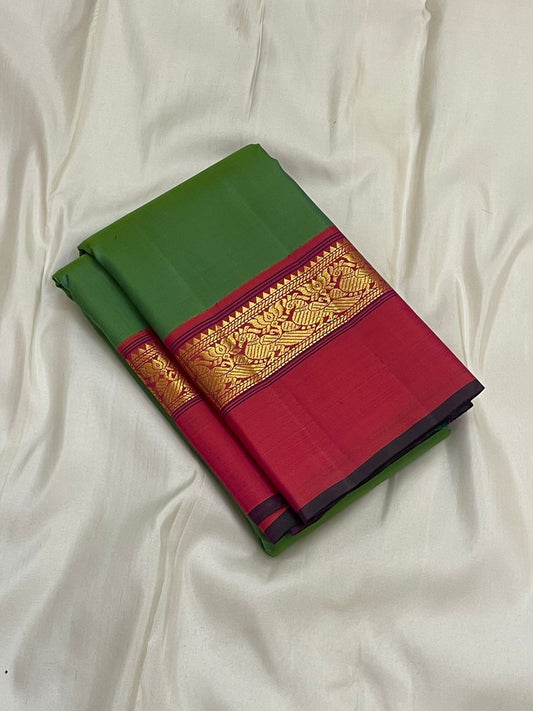 Folded green silk saree with wide pink border and gold zari woven band, placed on white fabric.