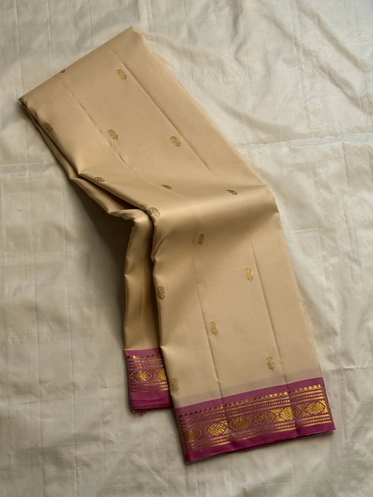 Cream silk saree draped loosely, showing scattered gold buttas and a magenta border with gold zari woven detailing.