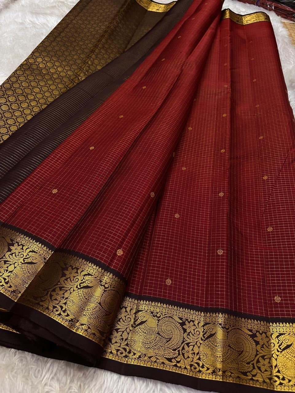 Mantra – Ruby Red coffee brown Kanchipuram Silk Saree with zari Checks with small buttas all over and Antique Peacock zari Border  showcasing regal peacocks and floral vines. A richly detailed pallu completes this heritage Zari kattam