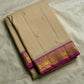 Folded cream silk saree with small gold buttas and a magenta border featuring gold zari woven motifs, on white cloth.