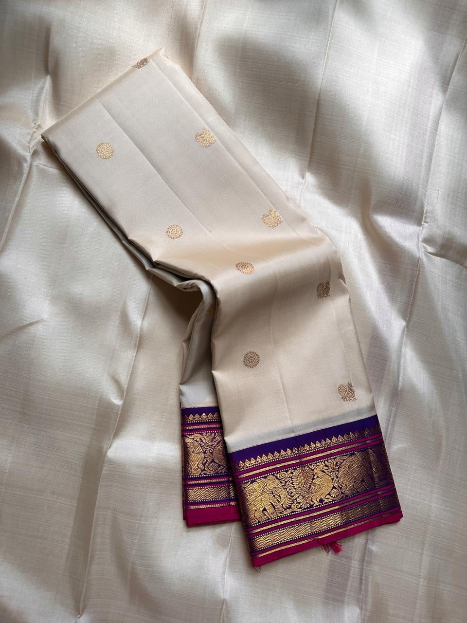 ⸻

Ivory Glow ✨ – Pure Kanchipuram Silk Saree in Ivory

Korvai Royal-Purple Border with Elephant & Peacock Zari Panels; Magenta Selvedge
Body with Gold Coin & Paisley Buttas
Grand Royal-Purple Brocade Zari Pallu with Hand-knotted Tassels