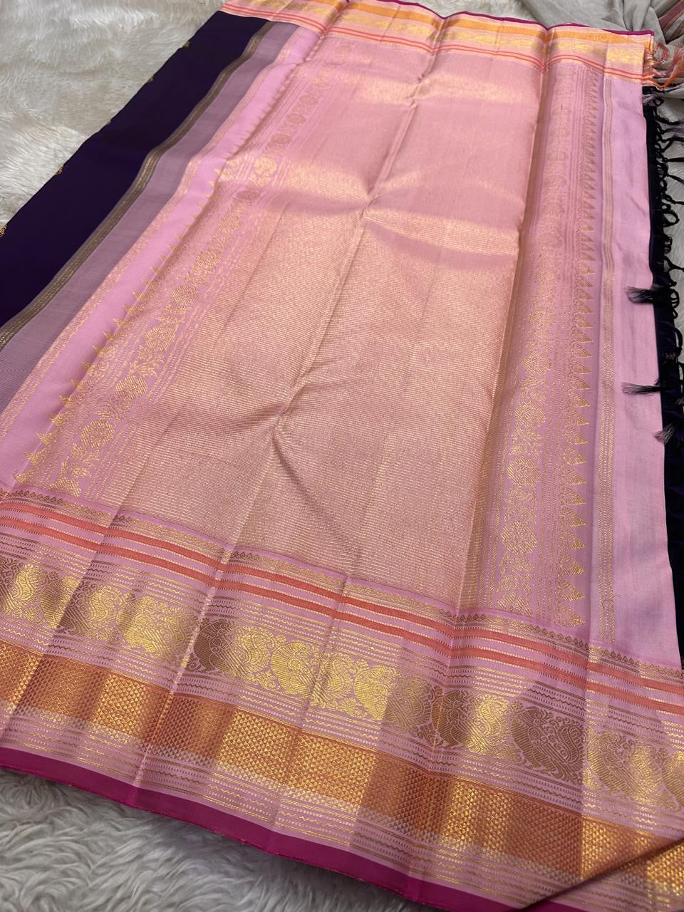 Shyamala—named after the deep, dark shade it embodies 💜 A pure Kanchipuram silk masterpiece with a rich purple body sprinkled with golden zari buttas. The contrast pink border glows with floral and paisley zari motifs, accented in coral and rose-gold, wh