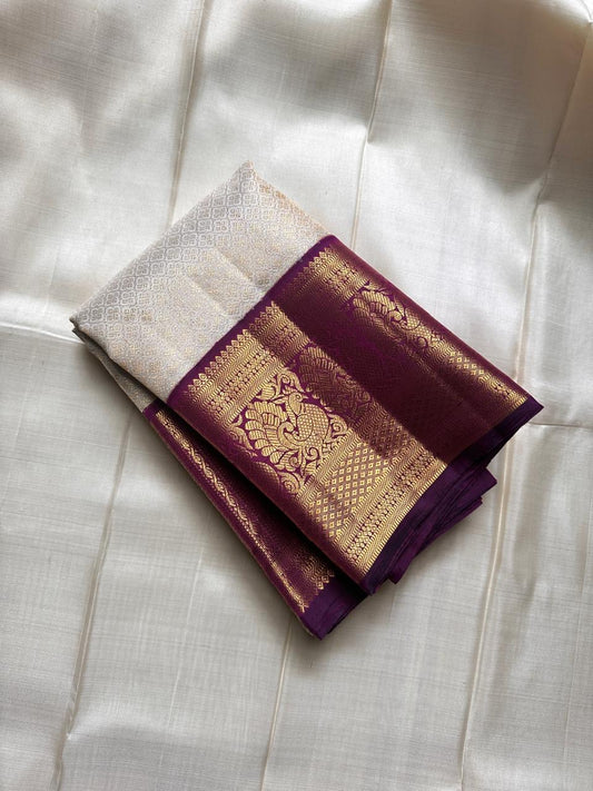 Ivory silk meets tradition in this elegant Kanchipuram saree. With a deep purple border and Mayuri motifs, it’s perfect for moments that call for quiet richness.