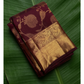 Maroon and gold saree with intricate patterns on a green leaf background