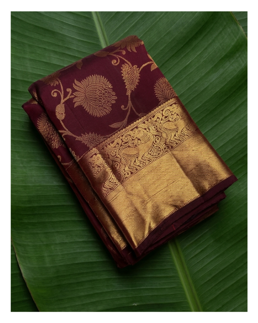 Maroon and gold saree with intricate patterns on a green leaf background