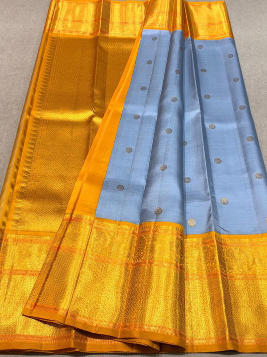 Eesha – Grey-Blue & Mustard Kanchipuram Pure Silk Saree.
Zari Butta All Over with Hamsa / Annapakshi   Motifs in Arai Maadam border . 
Detailed Chevron in pure 3g Zari Pallu with Muthu Seer Border for a Timeless Drape
