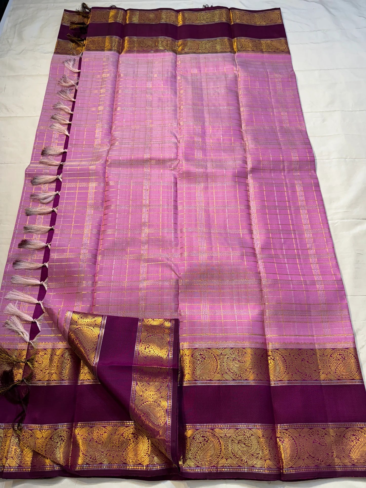 Mauve Mayil Mukham — Kanchipuram Pure Silk

Pastel-mauve pink  body with delicate zari wide kattam checks

Deep plum korvai border with grand mayil (peacock) chakram motifs

Copper-rose chevron zari pallu & plum contrast blouse

Silk Mark Certified • Free