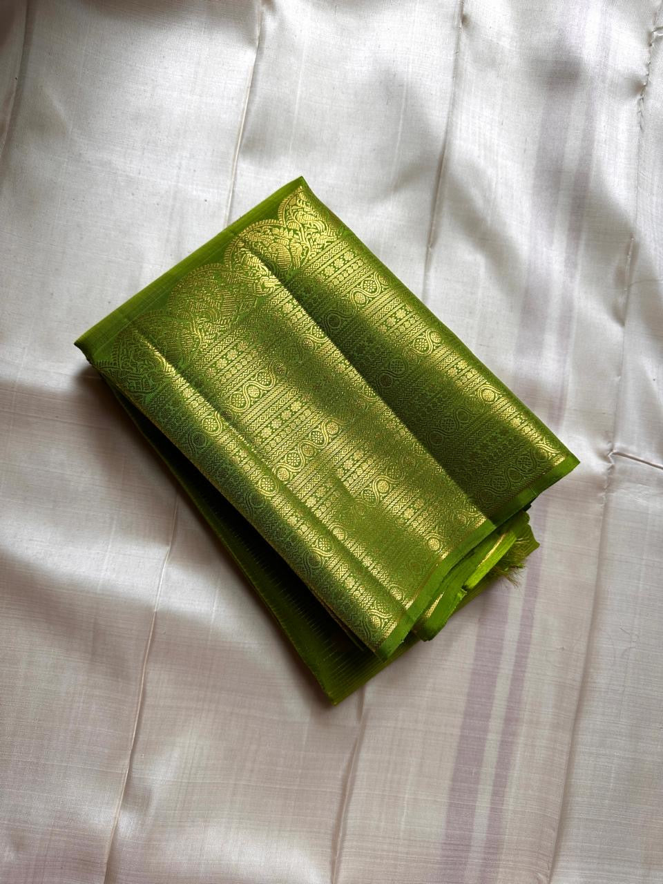 A radiant parrot green Kanchipuram silk saree that dazzles. The body features a delicate grid-like zari weave with small gold buttas scattered. The rich gold zari pallu stands out with grand temple-inspired arches and intricate motifs.