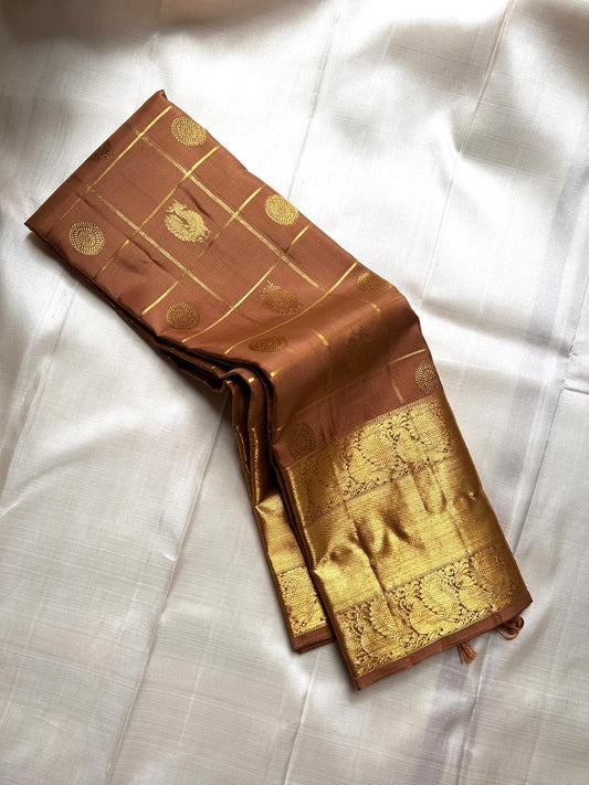 Bronze Chakram — Kanchipuram Pure Silk

Warm caramel-brown body with grid checks & “chakram” buttas

Grand gold zari peacock border & glowing pallu (kaddi + paisley vine)

Silk Mark Certified | Free Shipping within USA

Dispatch in 1 Week