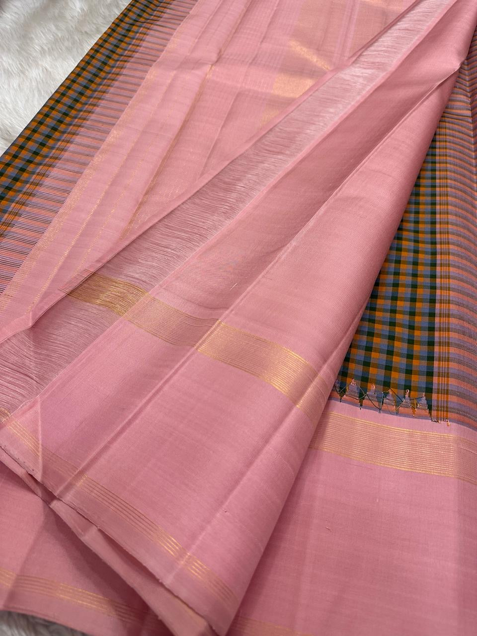 Nirai – A Madras-Inspired Kanchipuram Silk in Amber & Pastel Pink.
Woven with fine podi kattam checks in black, amber orange, and grey.
The pastel pink border with pillayar moggu detailing adds softness, with a  seer zari pallu