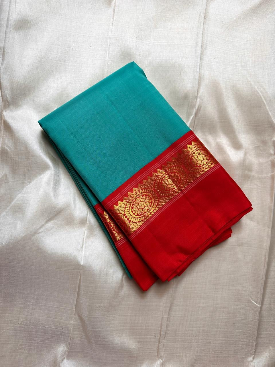 Rama green handloom Kanchipuram silk saree fully spread out, featuring rich red kaal erangina pallu and traditional gold zari motifs.
