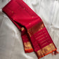 Partly opened pink-red Kanchipuram silk saree showing fine pinstripes, small gold buttas and gold lined border.