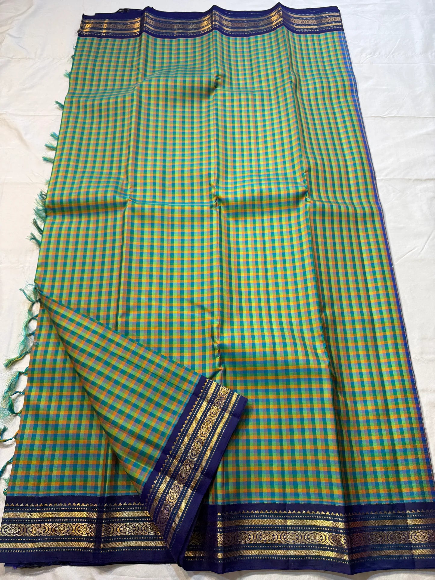 Mayil Pachai Kattam
Pure Kanchipuram Silk Saree – Peacock Green & Mustard Micro Checks
Royal blue korvai borders with gold floral zari detailing
Grand zari pallu with traditional zari weaving
Ships in two weeks free shipping, silk mark certified