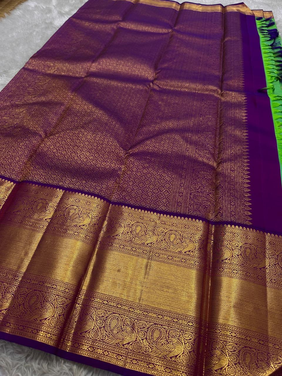 This pure silk Kanchipuram saree features a radiant shot color blend of green, gold, and blue, adorned with delicate zari buttas. A regal royal purple rettapet border and an elaborate peacock motif pallu complete this timeless drape — perfect for festive