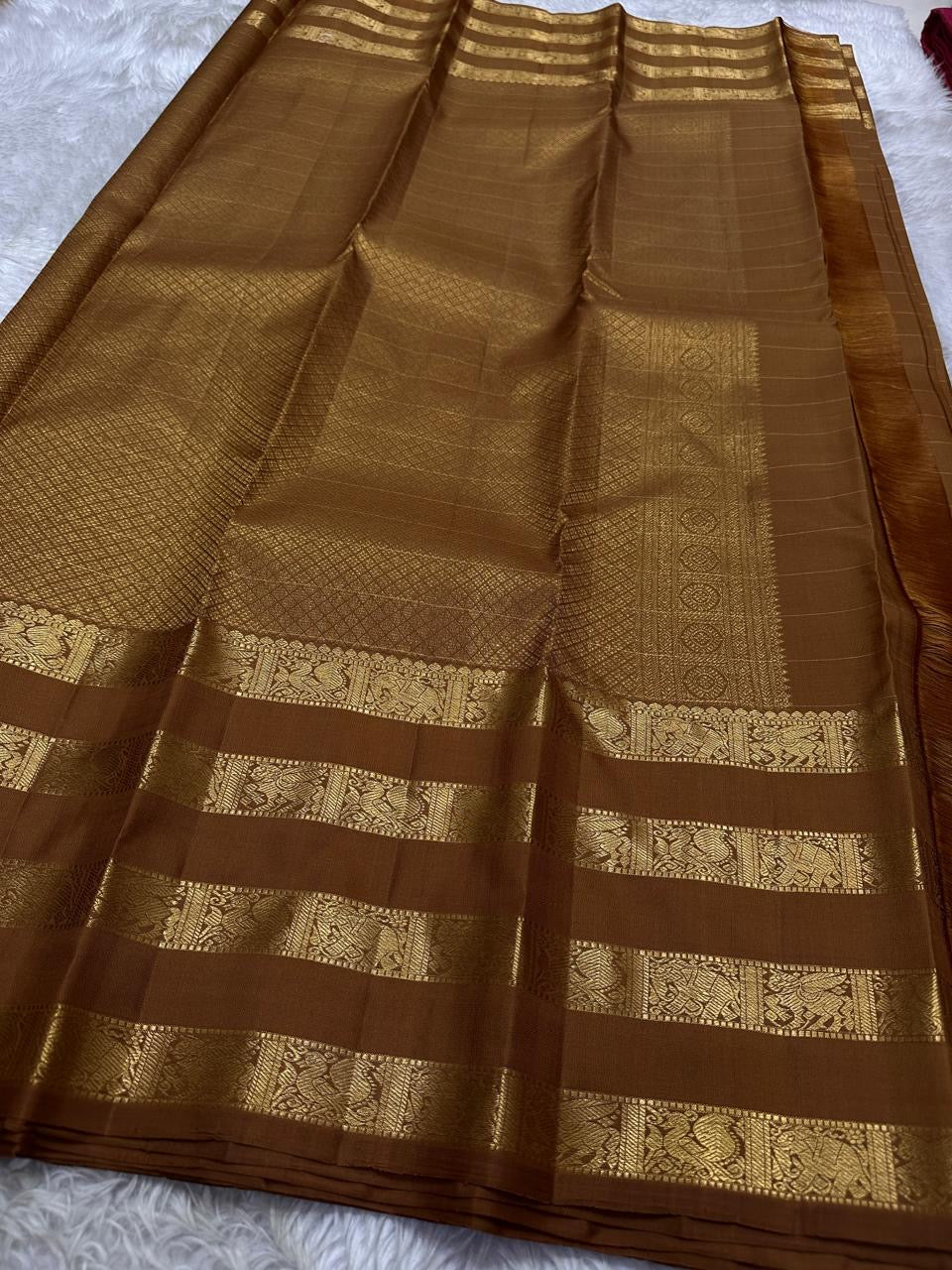 vasantham  Brown– Handwoven Kanchipuram Silk Saree A poem in Brown silk. The body glows in a serene earthy Brown, softly accented by delicate gold vertical lines and dainty gold zari buttas that glint like little blessings.