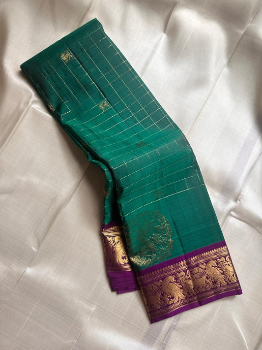 Sorgavaasal Kili – Pure Silk Kanchipuram Saree in Teal with Purple Zari Kattam
Intricately handwoven with traditional zari kattam checks and adorned with exquisite zari-woven Yazhi buttas, this saree features a vibrant teal body paired with a regal purple