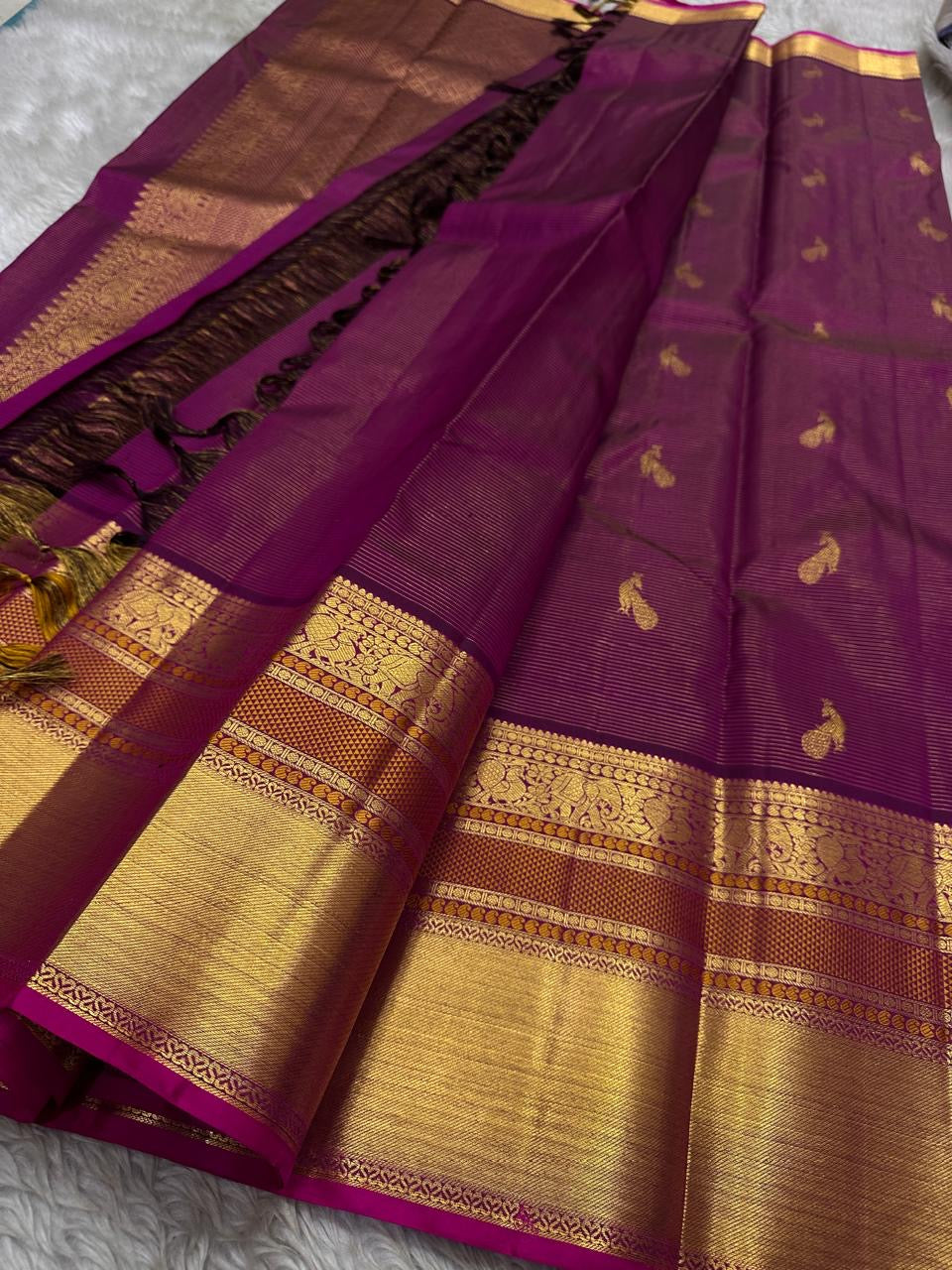 Angle view of magenta Kanchipuram saree showing gold zari border, peacock buttas and contrast pallu