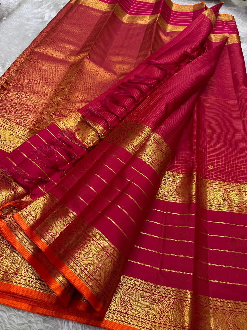 Open view of pink-red Kanchipuram silk saree with tasselled pallu, horizontal gold zari lines and ornate elephant border with orange selvedge.