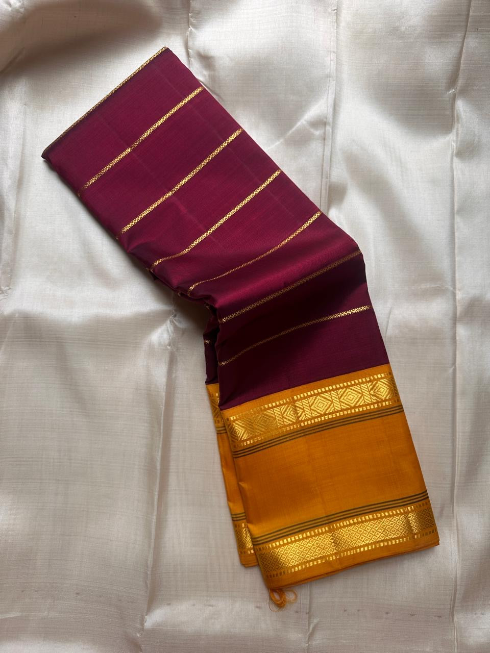 Half-folded deep maroon pure Kanchipuram silk saree with fine gold zari lines and mustard contrast zari border.