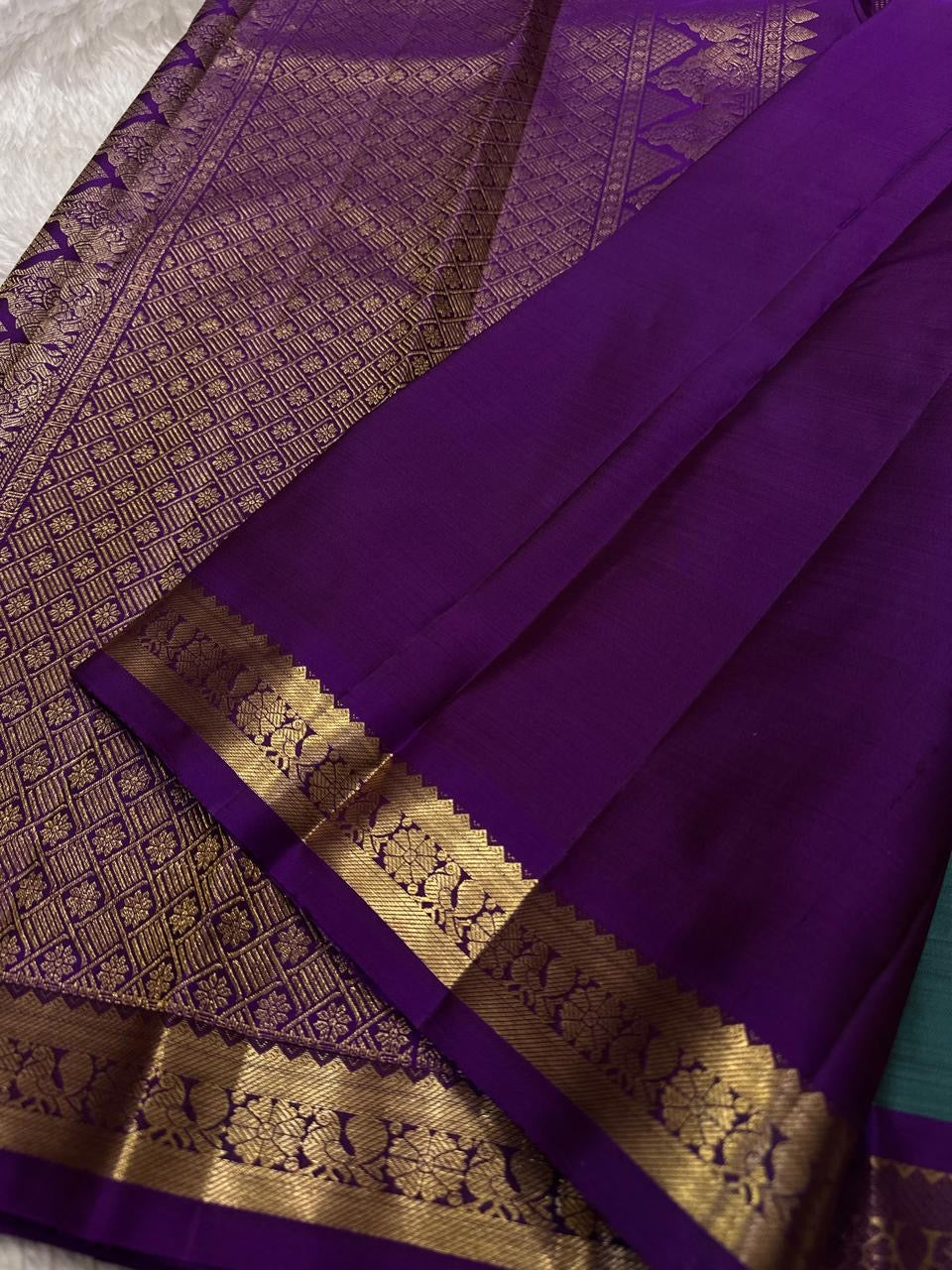 Close view of purple pallu with dense gold zari woven geometric pattern and a gold floral border.