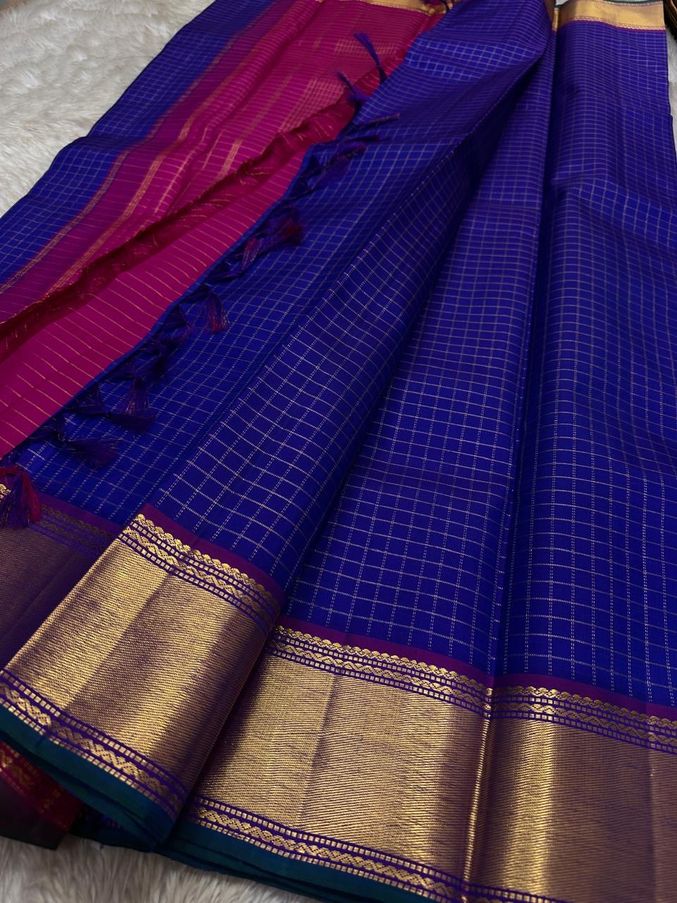Sapphire Zari Kattam – Pure Kanchipuram Silk Saree
Brilliant Sapphire Blue Body with Gold Zari Checks
Broad Golden Border with Magenta Highlights & Temple Motifs
Royal Magenta Pallu with Lustrous Zari Stripes

Silk Mark Certified, delivery in 2 weeks