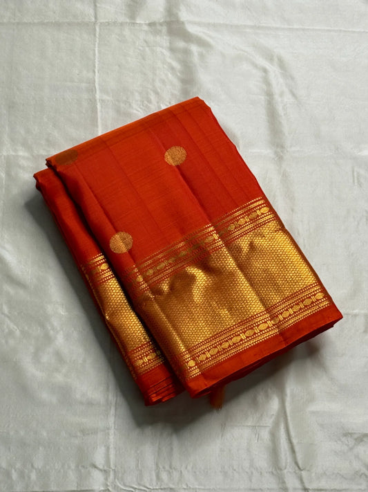 Maya
Vibrant Orange Kanchipuram Silk Saree with Lustrous Gold Coin Buttas
Handwoven Traditional Rudhraksham Seer and Intricate Arai Maadam Zari Border
Richly Crafted Pallu Featuring Elegant Gold Zari Panels for a Regal Finish