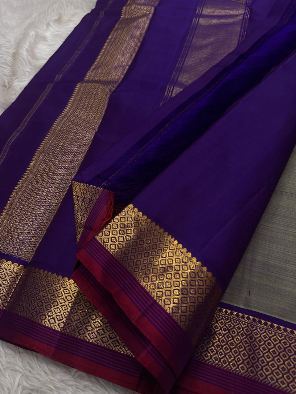 Varnam – Dove Tail Gray & Purple, a Kanchipuram silk saree where elegance meets bold expression. The soft dove tail gray base is adorned with vibrant magenta checks,Framed by a rich purple zari border and finished with an intricate contrast pallu