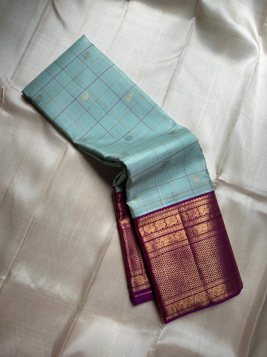 Shanti Blue – Pure Kanchipuram Silk Saree
Pleasant Blue Body with Purple Grid Checks & Zari Buttas
Deep Purple Korvai Border with Elephant & Floral Motifs
Majestic Zari-Dense Pallu in Traditional Weaving
Coordinated Blouse in Blue with Elegant Zari Border