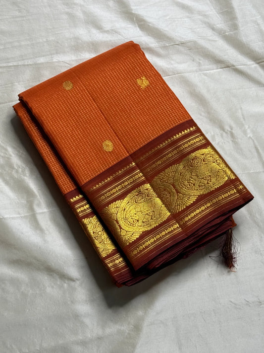 TEJAS – Vibrant Rust Orange Podi Kattam Kanchipuram Silk Saree

Micro-checks body with scattered gold chakram buttas; rich contrast maroon korvai borders

Grand circular annapakshi medallions in lustrous zari; ornate-jaal pallu & tassels

Silk Mark