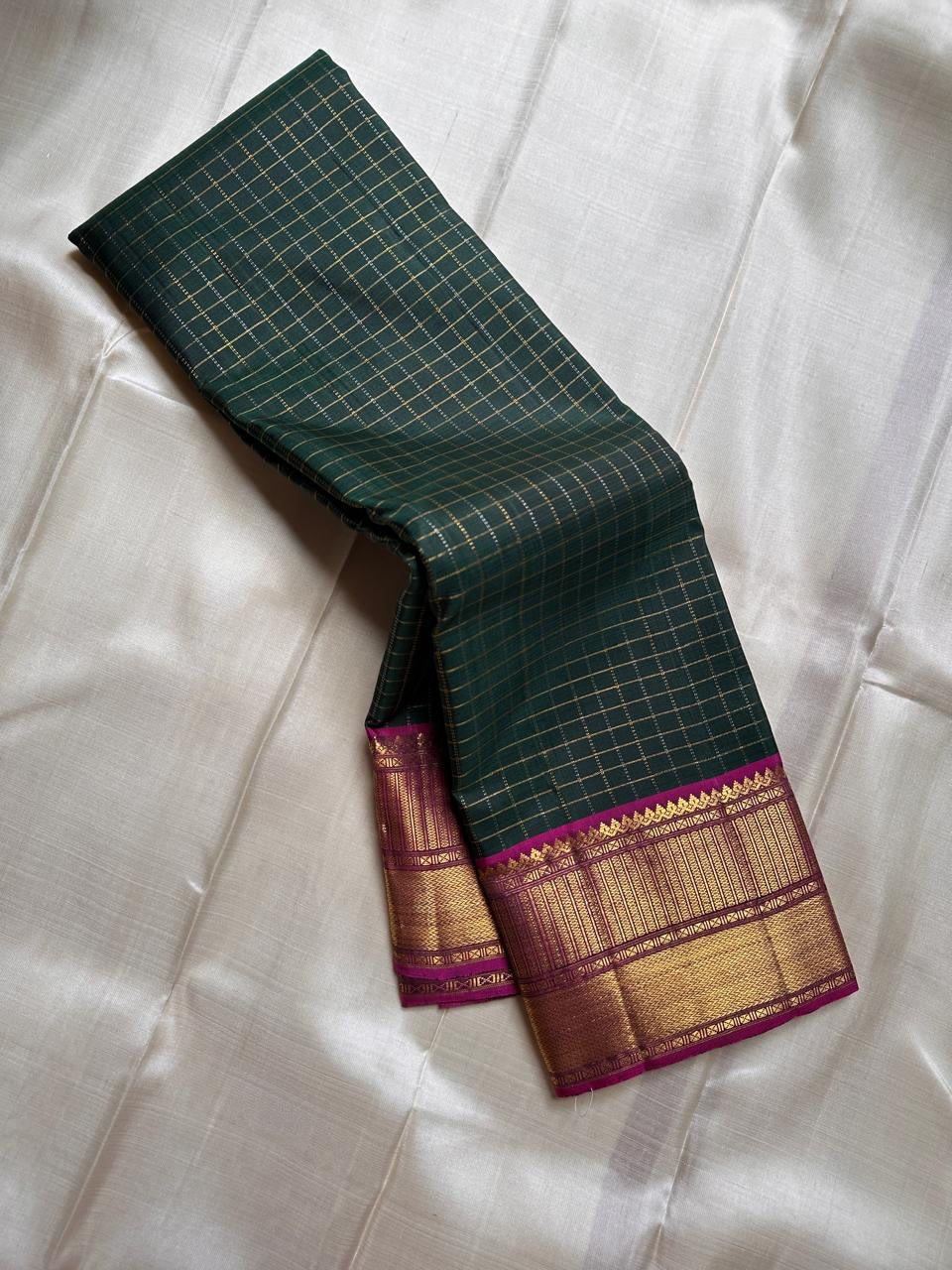 Pachai Zari Kattam – Pure Kanchipuram Silk Saree
Deep Emerald Green Body with Gold Zari Checks
Broad Golden Border with Magenta Highlights & Temple Motifs
Royal Magenta Pallu with Lustrous Zari Stripes

Silk Mark Certified, delivery in 2 weeks
